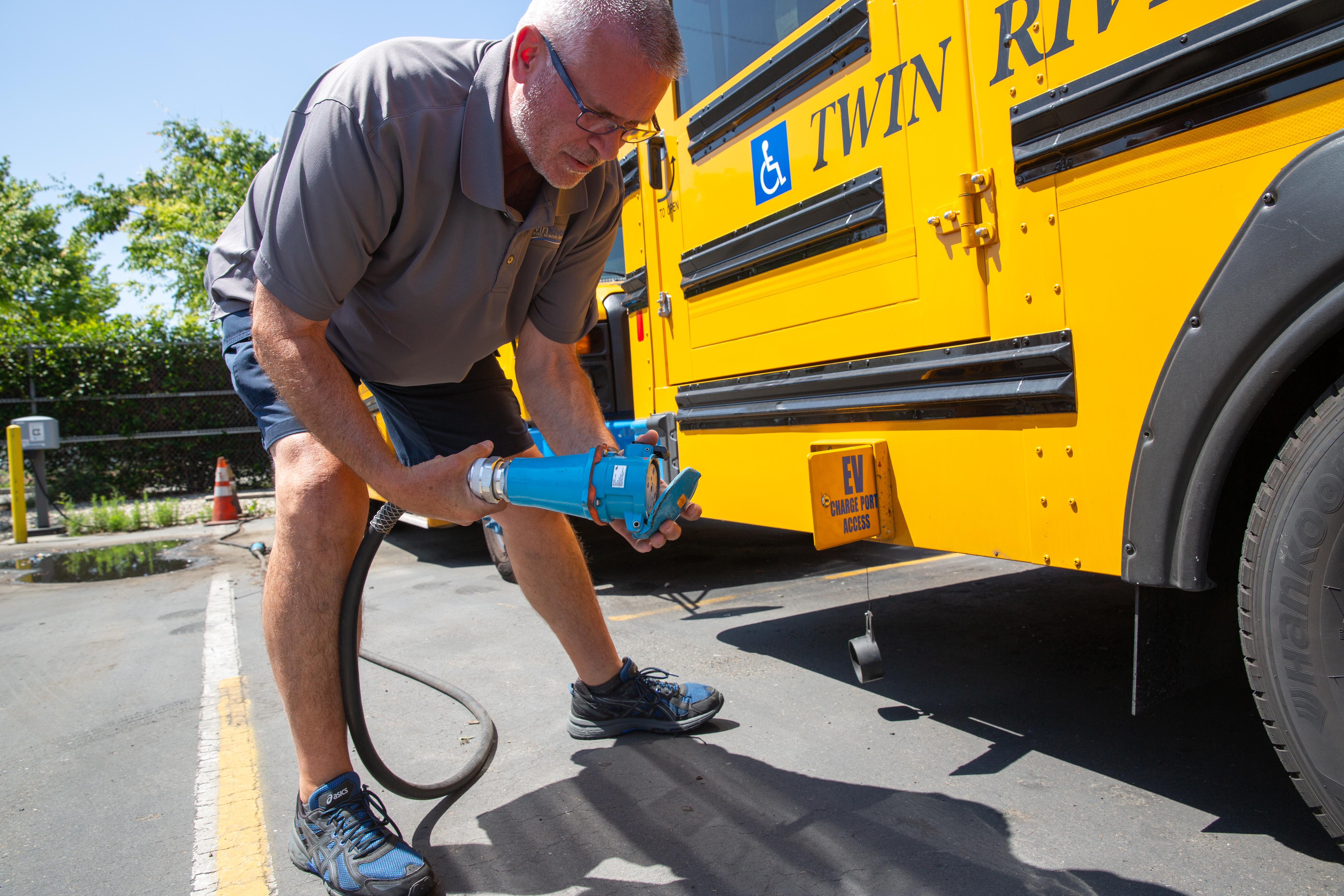 A man holds a charging nozzle near the charging port in a yellow electric school bus.