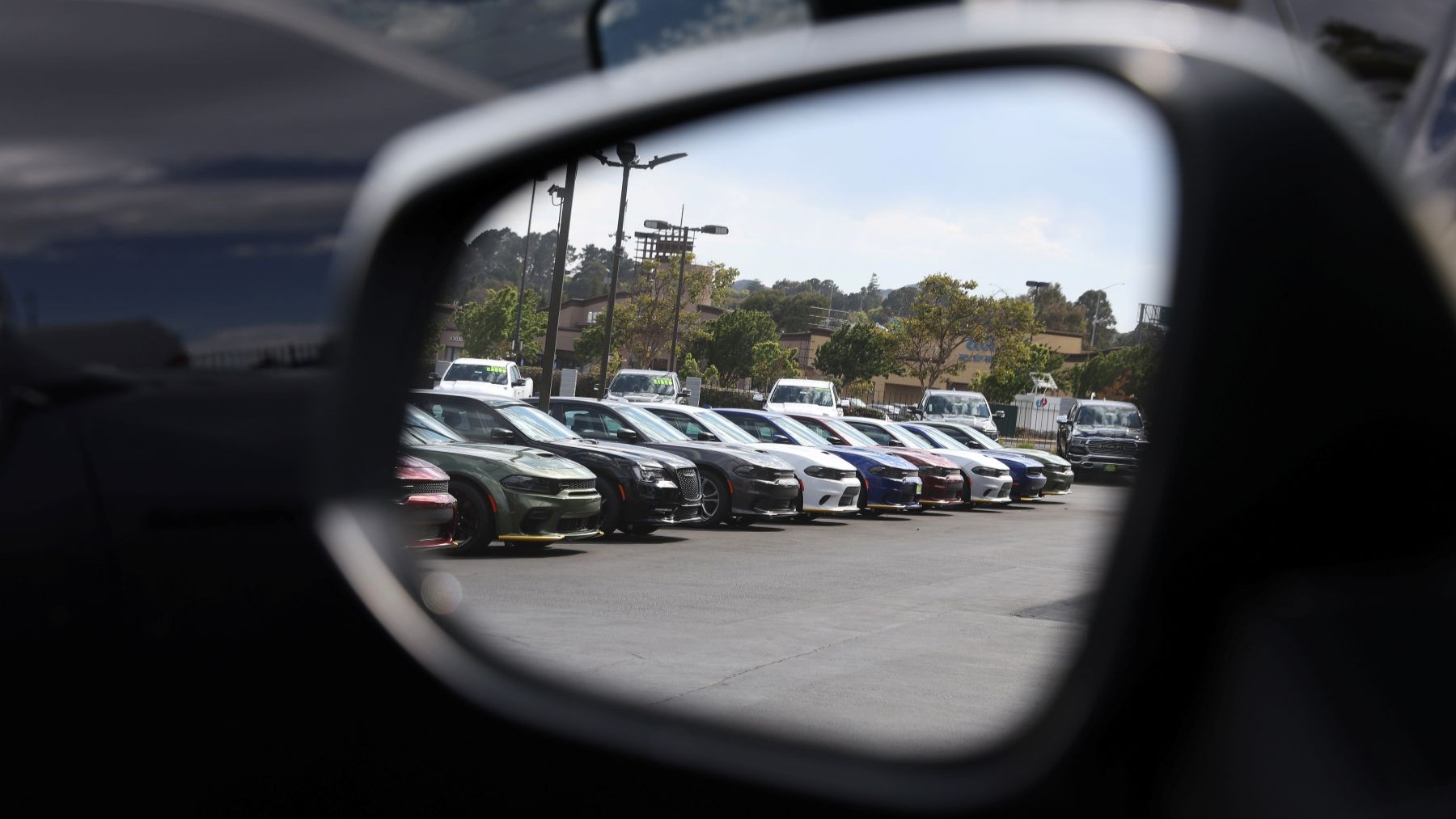 A line of electric vehicles in a parking lot seen through a rearview mirror
