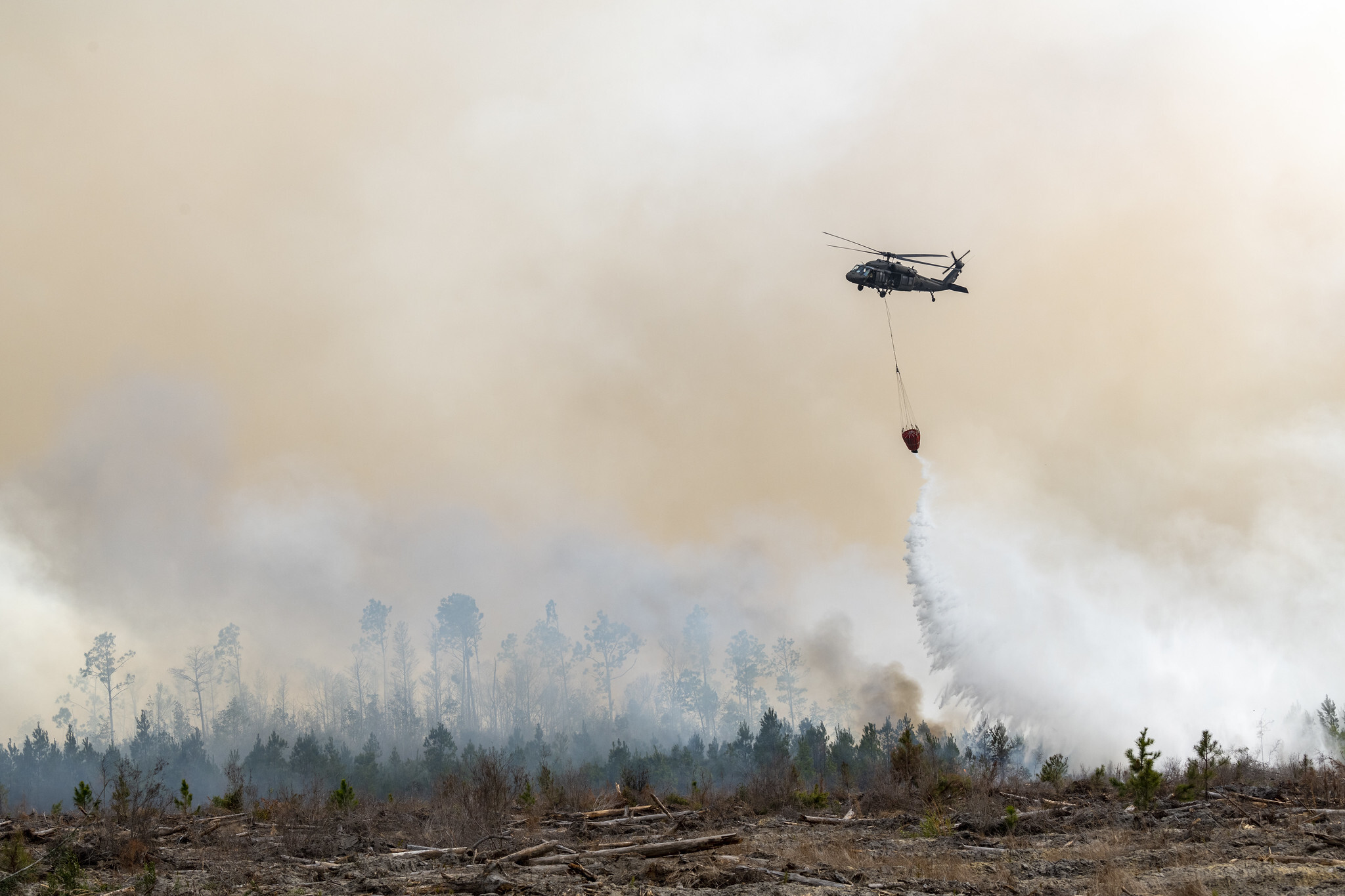A National Guard helicopter flying over burned trees and land in Florida to suppress the wildfire. 