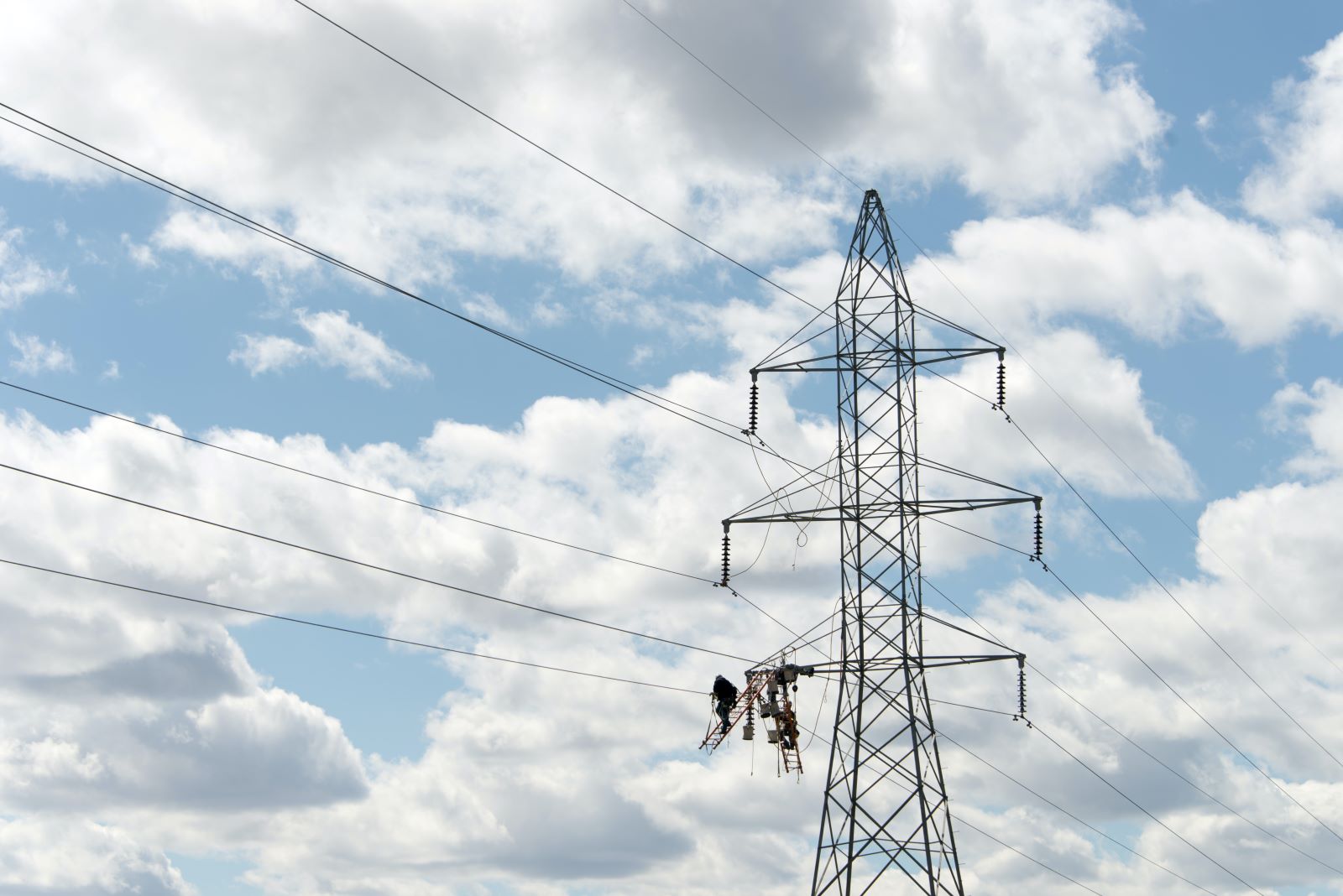 Clean energy workers servicing a high voltage transmission line on a bright but cloudy day.