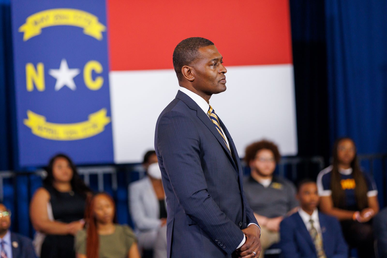 Administrator Michael Regan looks onward with a crowd and North Carolina flag behind him.
