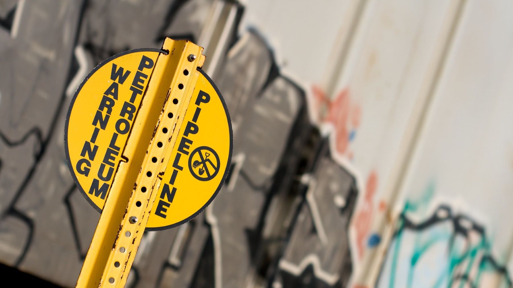 Yellow petroleum pipeline warning sign in front of graffiti