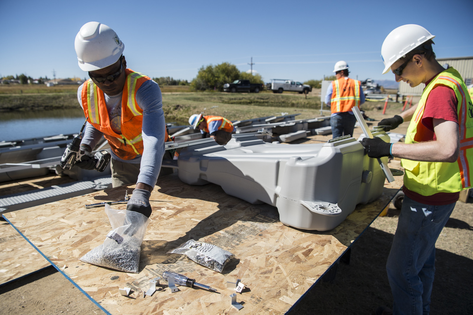 Close up of solar installation workers in vests and hardhats grabbing nuts and bolts to finish building a solar array in Colorado.