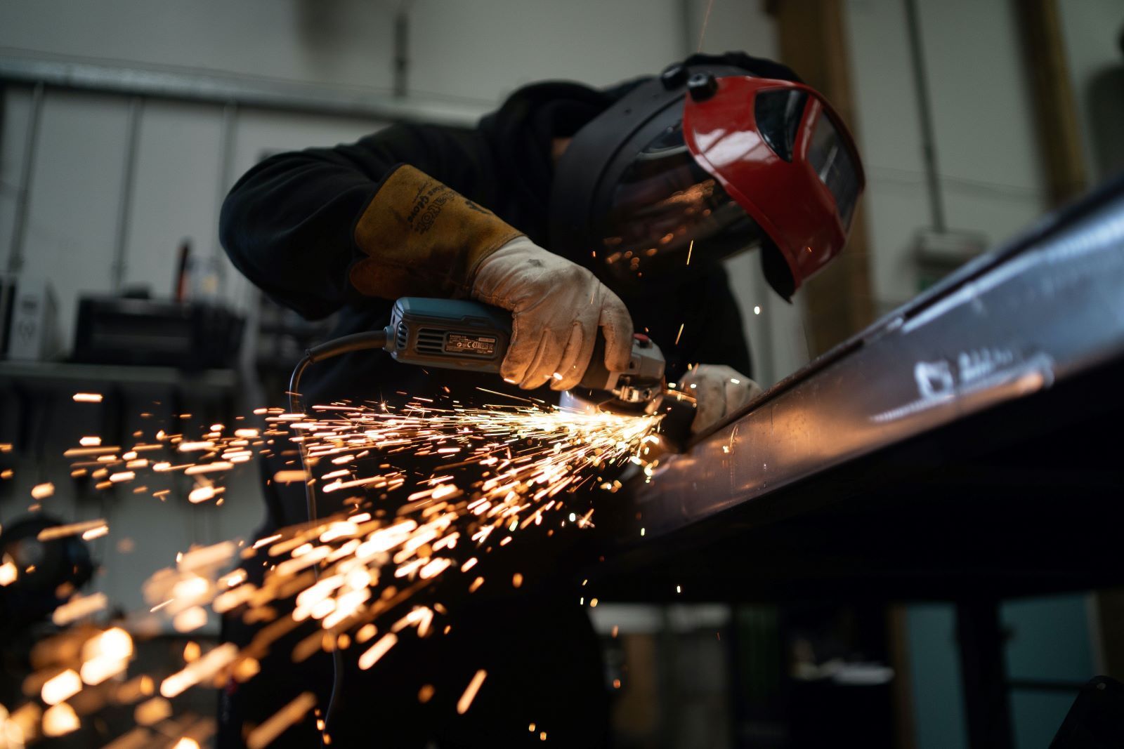 Person in protective gear using a small electric hand saw on a piece of metal. Sparks are flying off the metal.