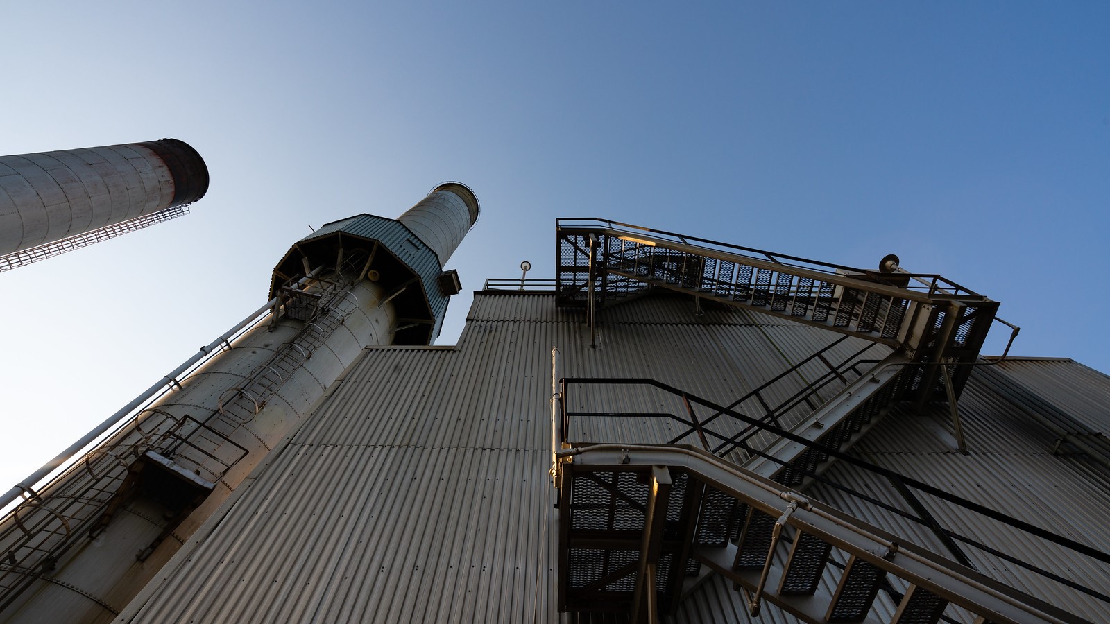 Low angle shot of a fossil fuel power plant smoke stack and facility.