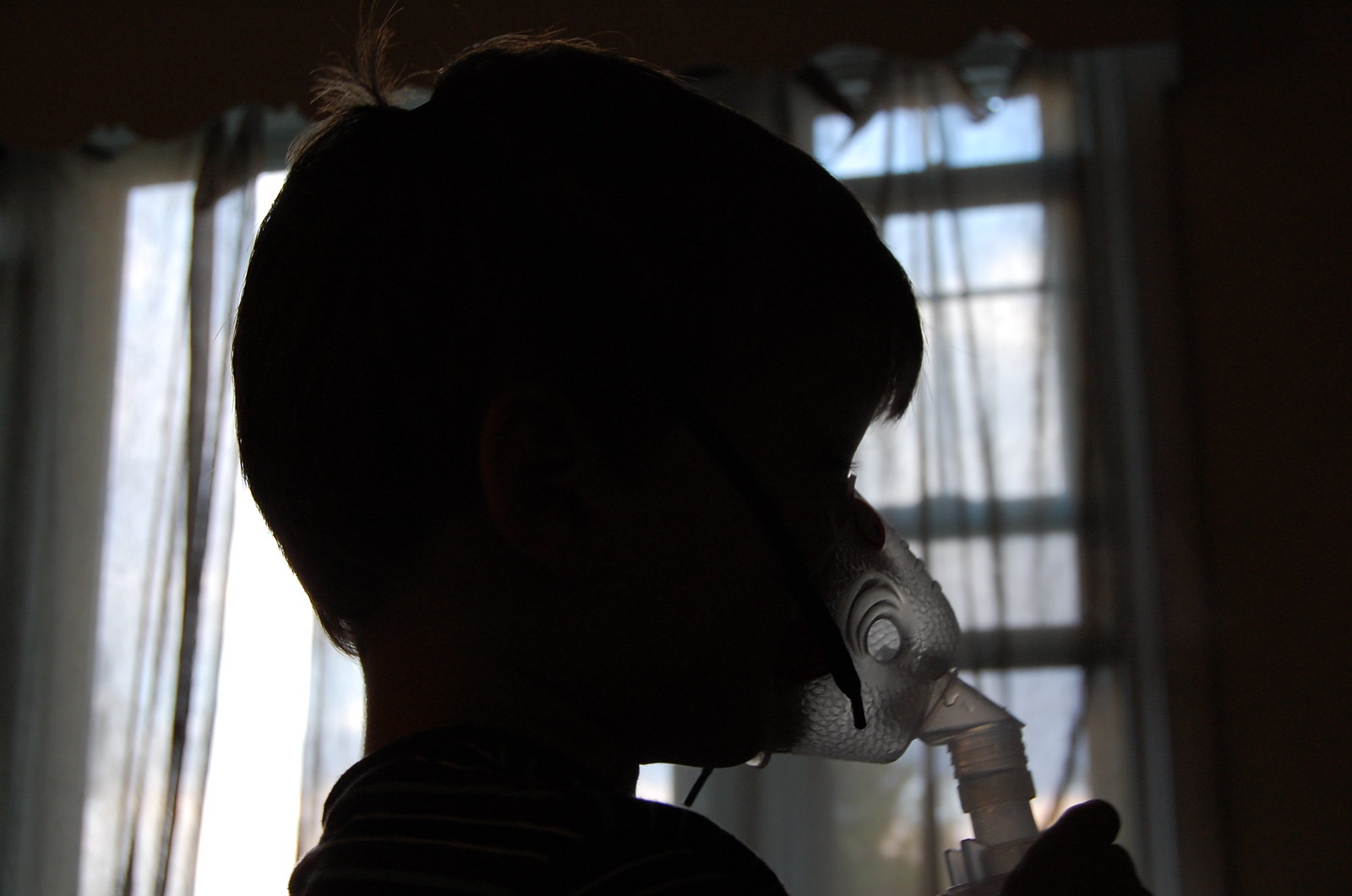 Silhouette of a child inhaling medicine from a nebulizer.