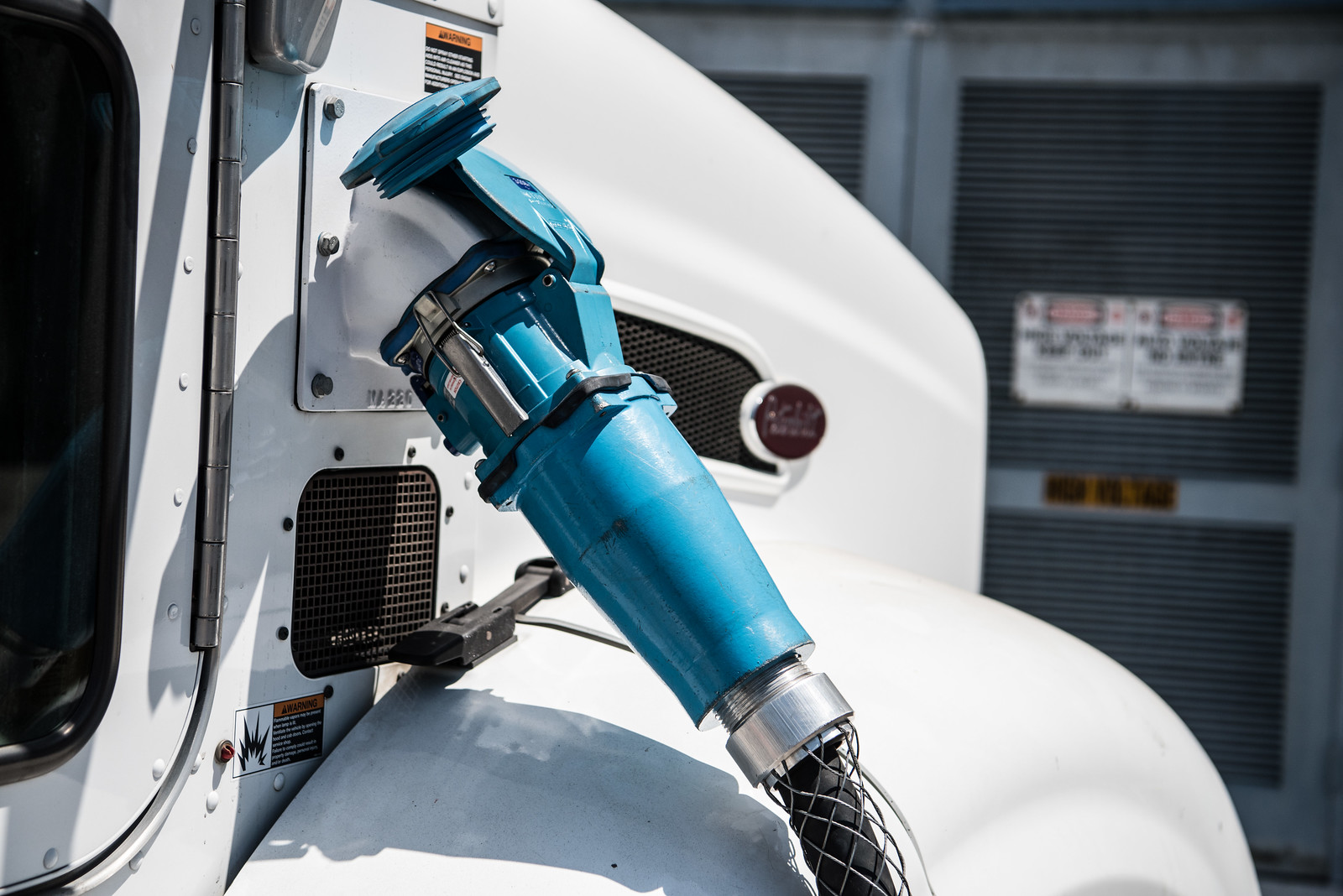 Close up of a blue electric charging cable plugged into a white truck.