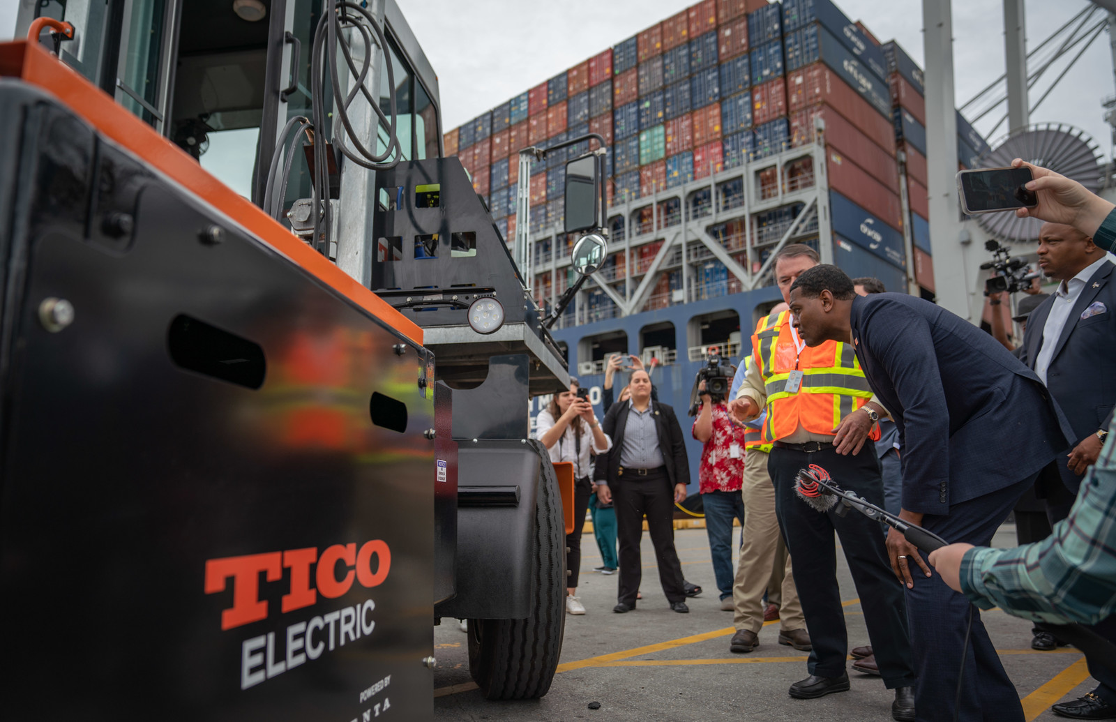 EPA Administrator Regan crouching to get a closer look at an all electric truck parked at a port.
