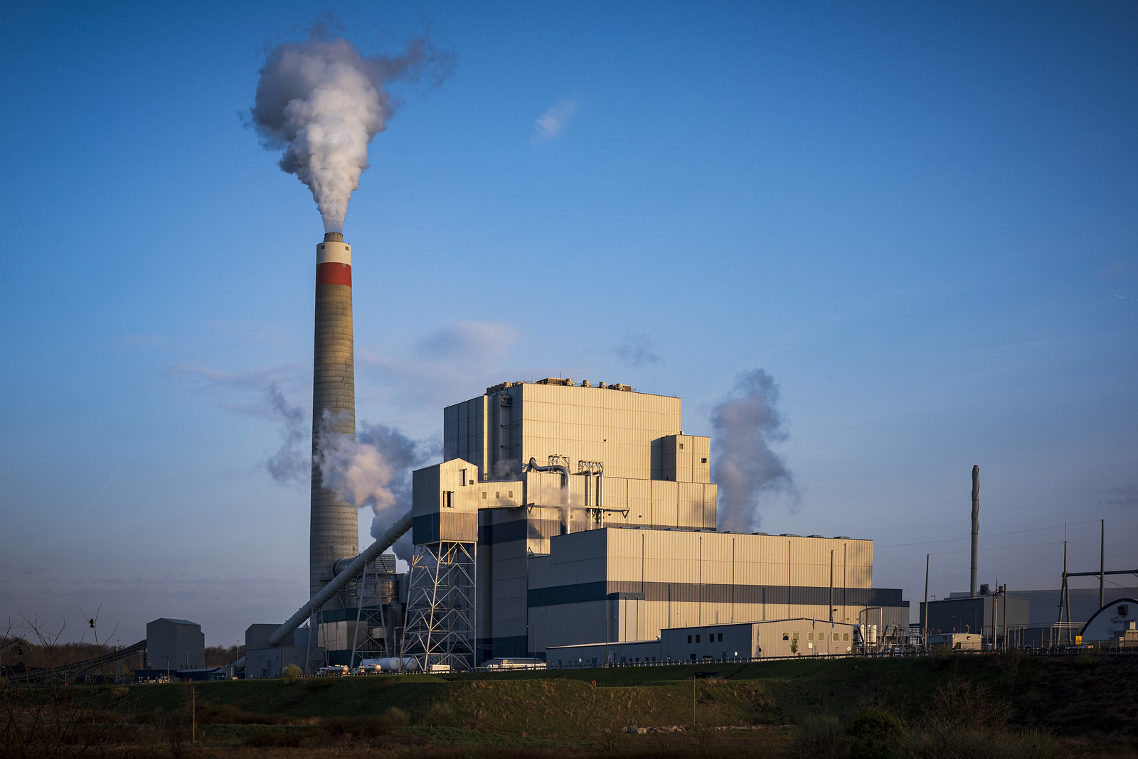 A wide angle shot of a white coal power plant spewing exhaust from its chimney.