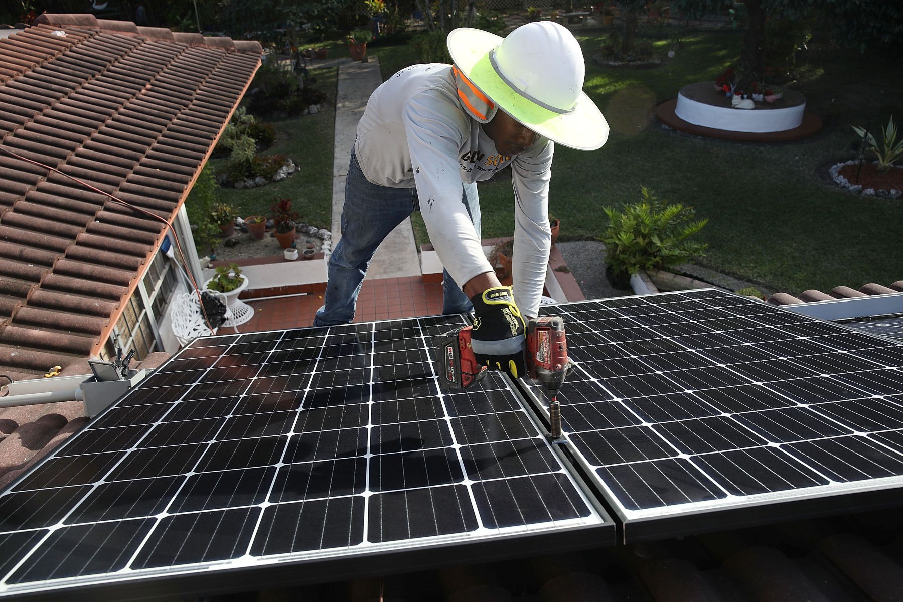 Person with white sun hat installing a solar panel system on the roof of a home