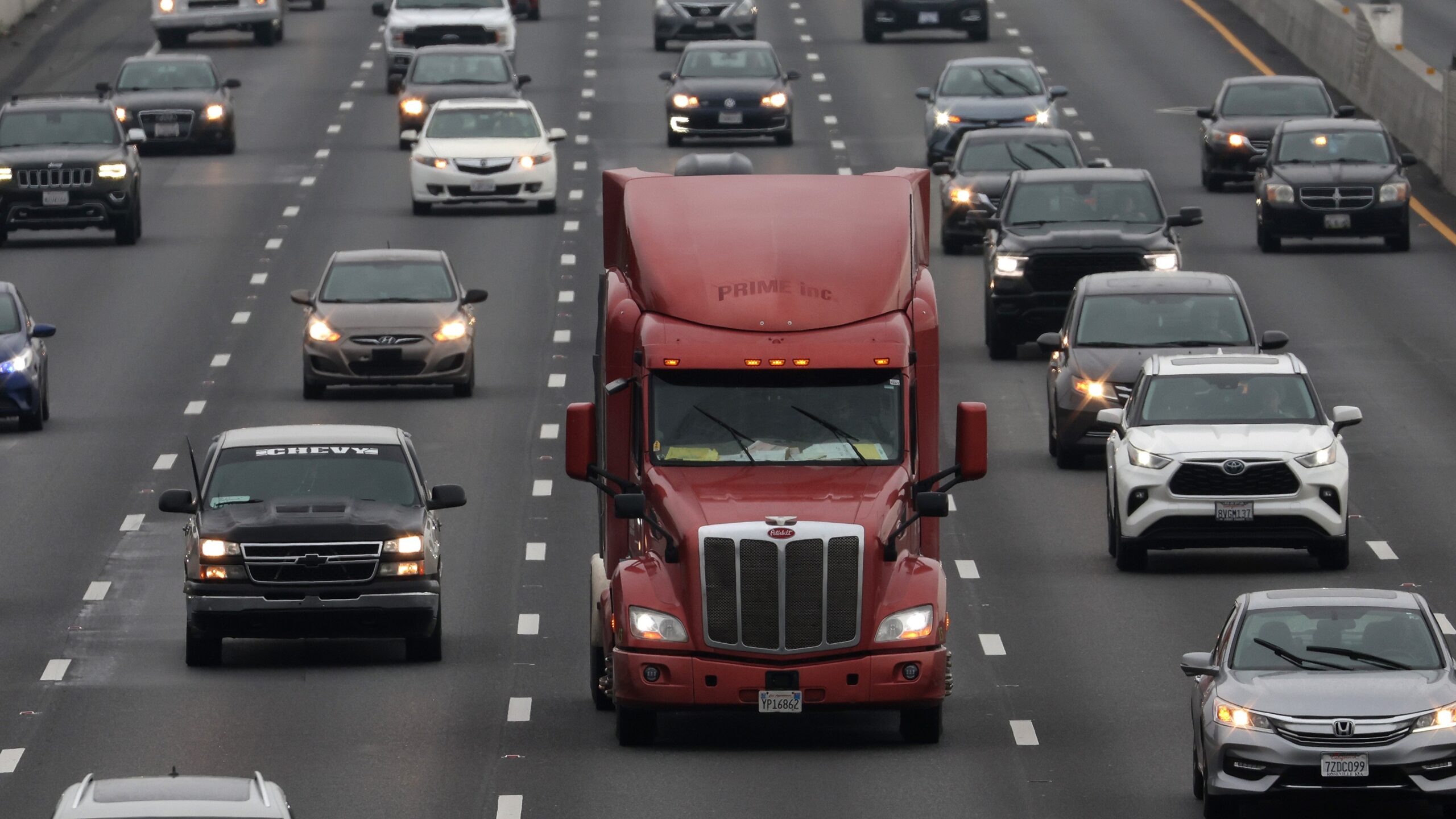 A red heavy duty truck driving amongst cars on the freeway