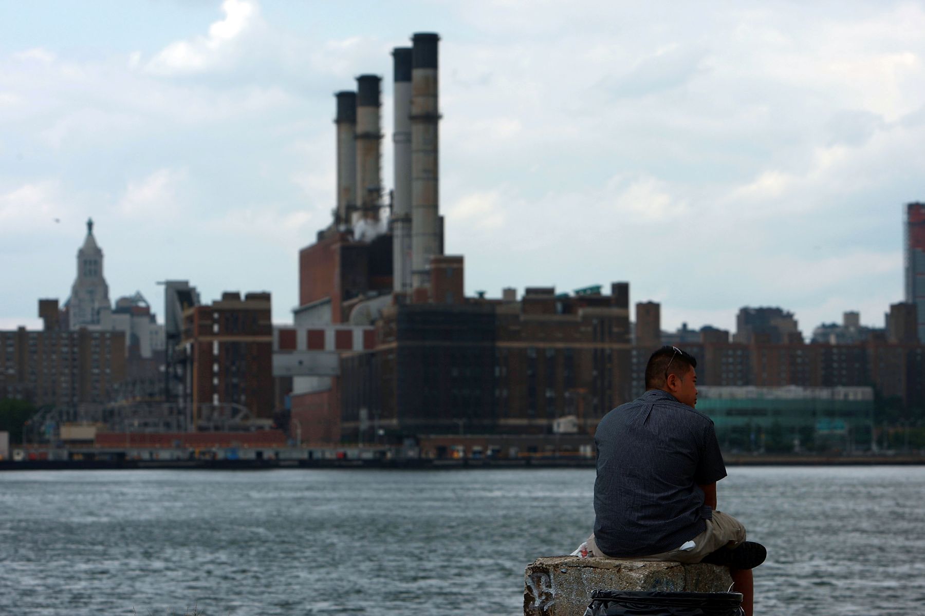 A man sits across the river from a Con Edison power plant in New York City. 