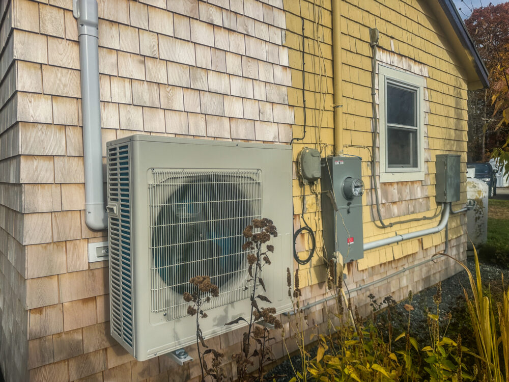 A Mini-Split AC Unit, Heating and Cooling System, mounted on an old home with yellow and cream-colored siding