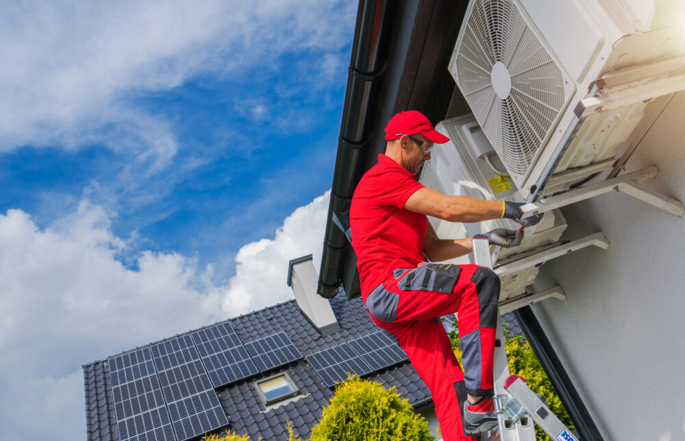 A man installs a heat pump on the outside of a building