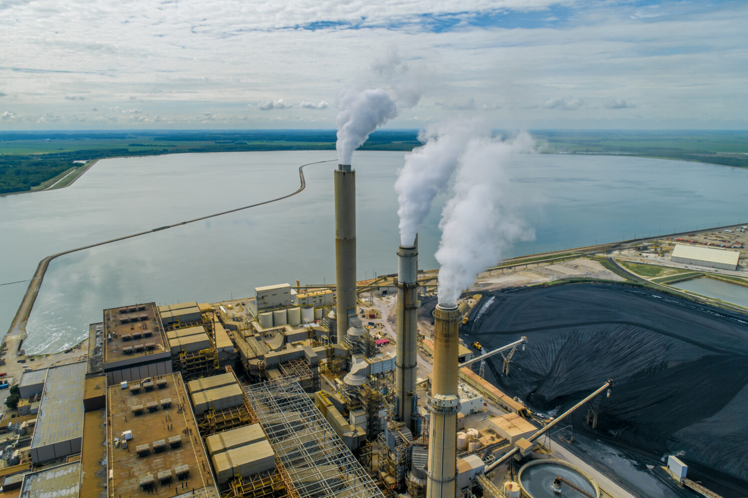 Aerial view of a large coal-fired power plant, which is situated near a large body of water.