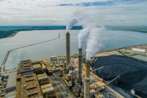 Aerial view of a large coal-fired power plant, which is situated near a large body of water.