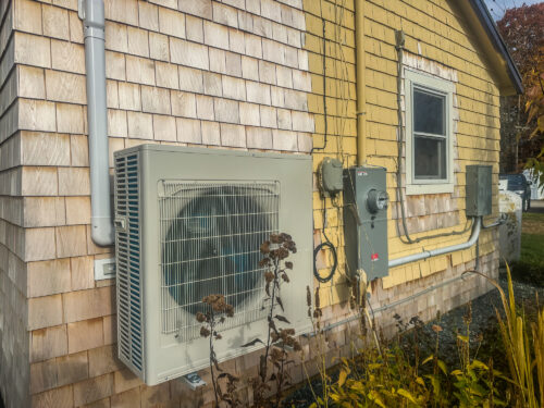 A Mini-Split AC Unit, Heating and Cooling System, mounted on an old home with yellow and cream siding